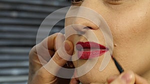 Female make-up artist apply pink lipstick with brush on a client lips