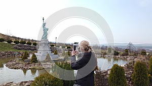 Female makes photo walking on foot near a miniature model of the Statue of Liberty, New York City. Park of Miniatures.