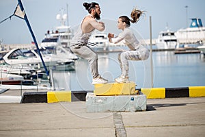 Female and male athlete is performing box jumps outdoor.