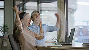 Female and male co-workers reading email on laptop and becoming extremely happy