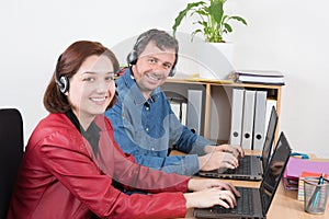 Female and male customer service agent wearing headset with colleagues working in background at office
