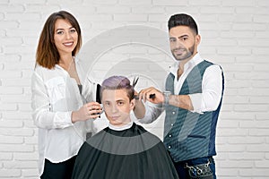 Female and male hairstylists doing haircut for young client with toned hair.