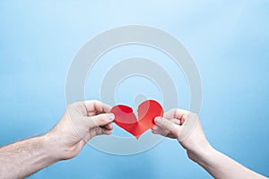 Female and male hand break a paper red heart on a blue background with place for text. Relationship problems