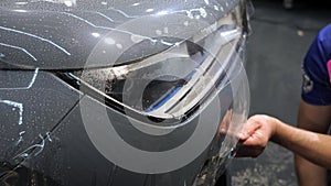 Female and male hand with plastic scrapers glue the protective film on the bumper.