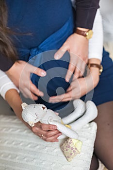 Female and male hands holding the belly of a pregnant woman. Pregnant wife in a blue dress. Father and mother are holding a white