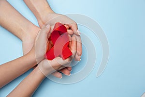 Female and male hands holding red HIV and AIDS awareness ribbon isolated on blue background