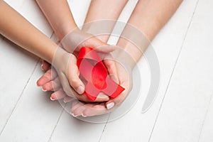 Female and male hands holding red HIV and AIDS awareness ribbon isolated on wooden background