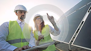 A female and a male solar inspectors are having a discussion near a solar module. Green energy concept.