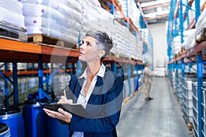 Female manager checking stocks on clipboard in warehouse