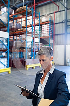 Female manager checking stocks on clipboard in warehouse