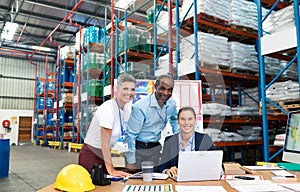 Female manager with her coworkers discussing over laptop at desk in warehouse