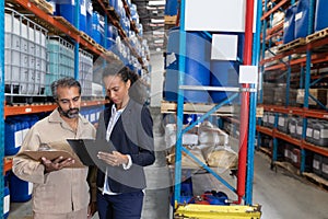 Female manager and male worker discussing over clipboard in warehouse