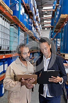 Female manager and male worker discussing over clipboard in warehouse