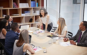 Female manager stands addressing team at boardroom meeting