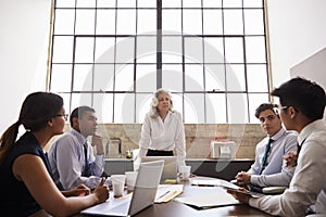 Female manager stands listening at team brainstorm meeting