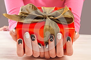 Female manicured hands and gift box.