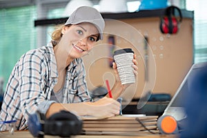 female manual worker with takeaway coffee working in workshop