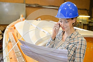 Female marine carpenter holding blueprint and taling on phone