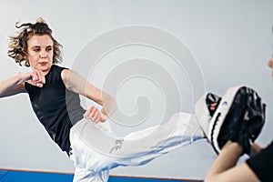 Female martial arts fighter practicing with trainer, punching taekwondo kick pad exercise kicking. Training of kickboxer woman
