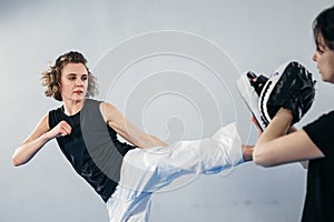 Female martial arts fighter practicing with trainer, punching taekwondo kick pad exercise kicking. Training of kickboxer woman