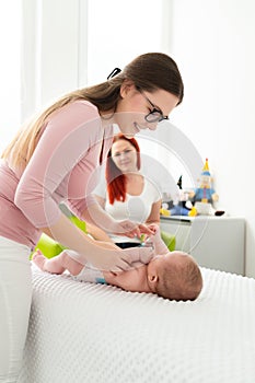 Female massage therapist or a doctor examining newborn baby boy with the mother watching in the background. Baby massage concept.