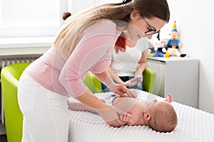 Female massage therapist or a doctor examining newborn baby boy with the mother watching in the background. Baby massage concept.