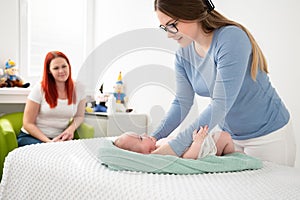 Female massage therapist or a doctor examining newborn baby boy with the mother watching in the background. Baby massage concept.