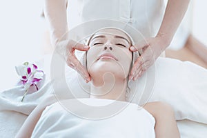 Female massage therapist giving a massage at a spa. Young woman receiving head and facial massage in spa salon