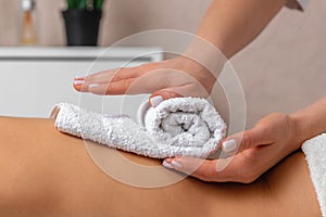 Female masseur hands putting white towel on the back of young woman enjoying treatment procedure in spa salon, atmosphere of calm