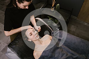 Female masseur standing next to a woman, giving her a gua sha face massage