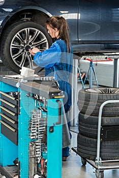 Female Mechanic Changing Tire From Suspended Car In Garage