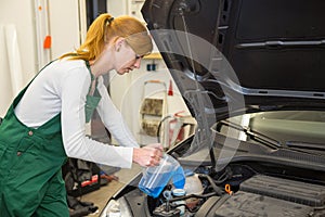 Female mechanic fills coolant or cooling fluid in motor of a car