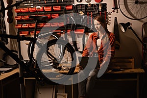 Female mechanic in her Workshop or garage looking at laptop. Bike shop owner with laptop.