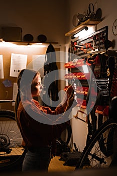 Female mechanic repairing bicycle in workshop, woman standing near wall with tools in garage. Bicycle maintenance