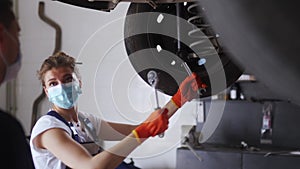 Female mechanic repairing the car suspension. Strong woman coaching a male trainee and working with socket wrench with