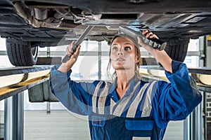 Female Mechanic Using Flashlight While Repairing Car On Lift