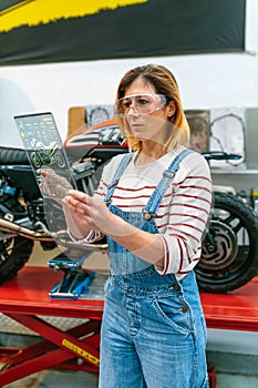 Female mechanic using transparent digital tablet with motorcycle diagnosis app