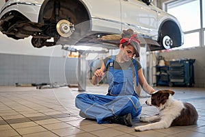 Female mechanik cuddle nice dog in car workshop