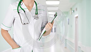 Female medical doctor with clipboard standing over blurry hospital background