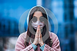 Female in medical mask praying outdoors in the empty city. Health protection and prevention of virus outbreak, coronavirus, COVID-