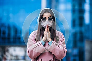 Female in medical mask praying outdoors in the empty city. Health protection and prevention of virus outbreak, coronavirus, COVID-