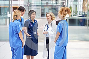 Female Medical Team Having Informal Meeting Standing In Lobby Of Modern Hospital Building