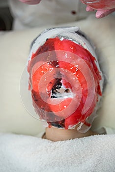 female medical worker applying on face red alginate mask her client in beauty salon