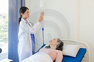 A female medical worker in Asia visits an elderly woman lying in bed to inquire about the patient's condition