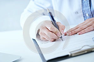 Female medicine doctor hand holding silver pen writing something on clipboard closeup. Lot of paper work in medicine