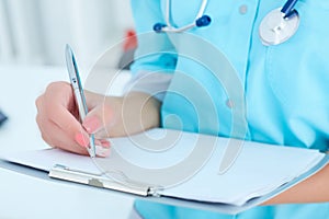 Female medicine doctor hand holding silver pen writing something on clipboard closeup.