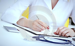 Female medicine doctor hand holding silver pen writing something on clipboard and working laptop closeup. Physician