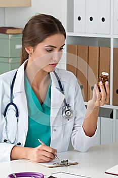 Female medicine doctor holding bottle with pills and writing prescription