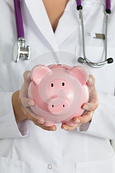 Female medicine doctor holding piggy bank