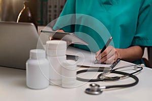 Female medicine doctor, physician or practitioner in lab room writing on blank notebook and work on laptop computer.